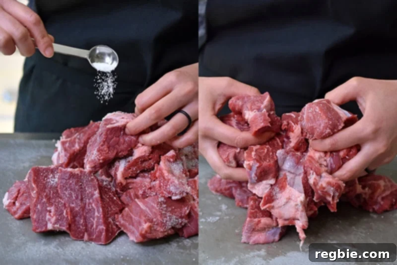 A shot of someone tossing cubed chuck roast with kosher salt on a gray cutting board, preparing it for cooking.