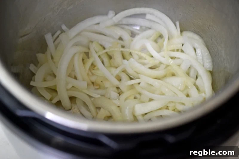 A closeup shot of the interior of an Instant Pot filled with sautéed sliced onions, showing their softened texture.