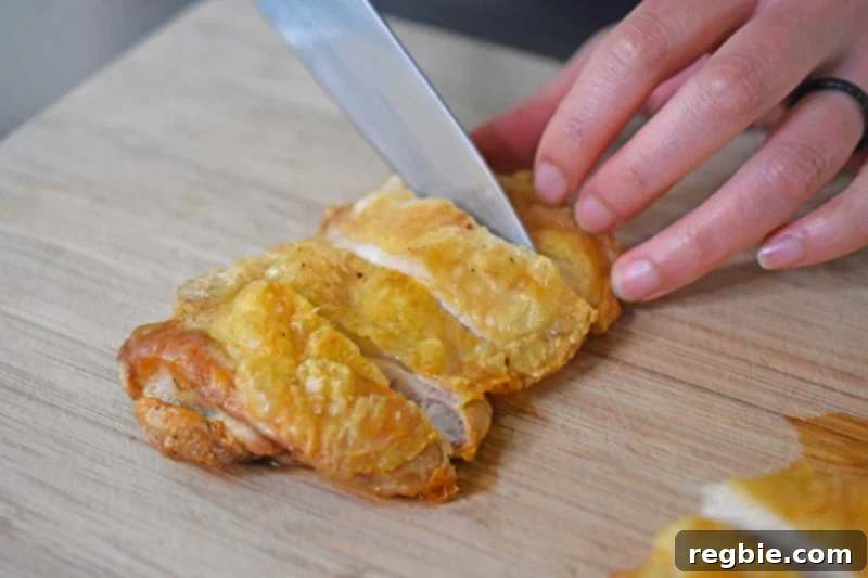 Ultimate Crispy Air Fryer Chicken Thighs 11 Slicing Air Fryer Cracklin' Chicken on a wooden cutting board, revealing its juicy interior and crispy skin.