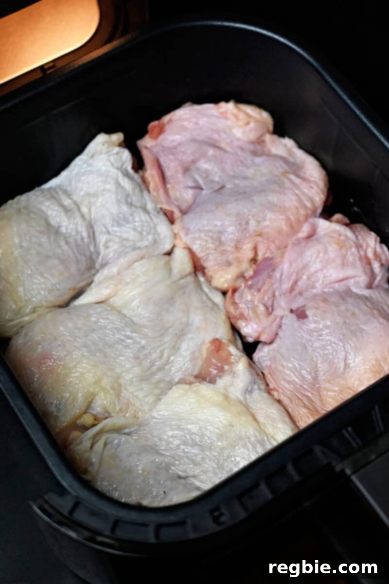Ultimate Crispy Air Fryer Chicken Thighs 9 An overhead shot showing five raw, seasoned chicken thighs arranged in a single, non-overlapping layer inside an air fryer basket.
