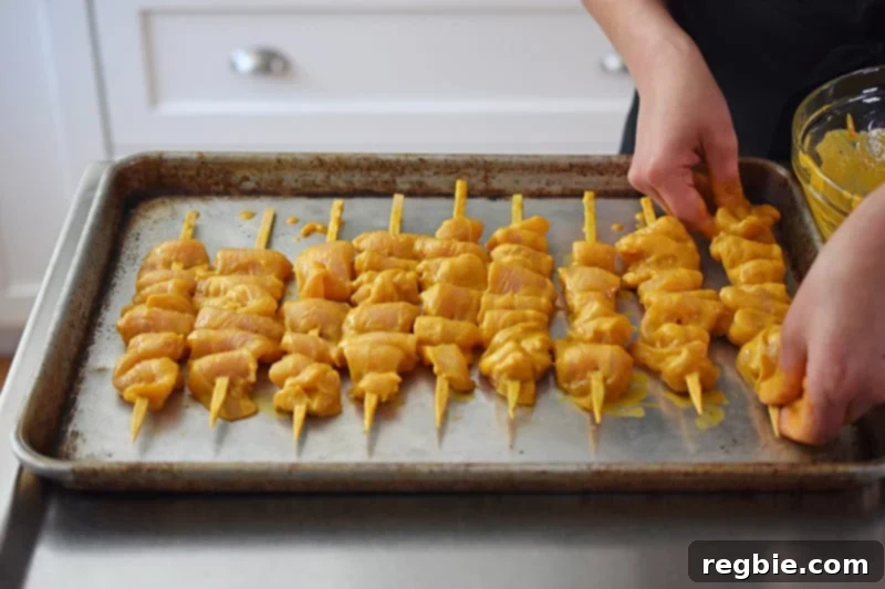 Placing the raw chicken satay skewers on a rimmed baking sheet before baking in the oven for an easy cooking option.