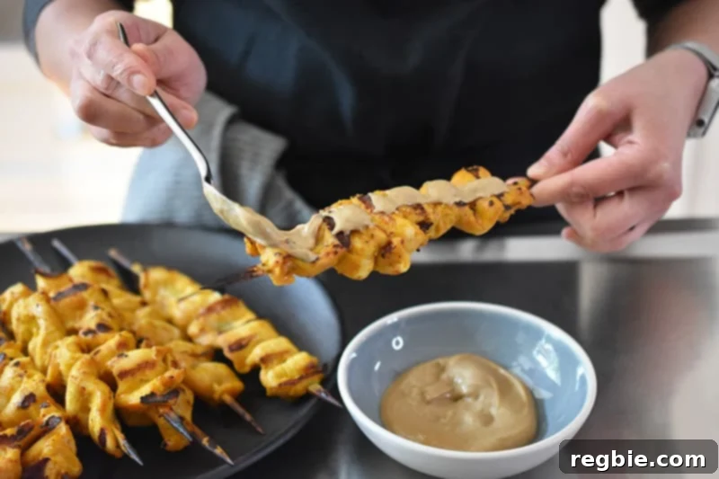 Someone spooning Hoisin No-Nut Sauce on Chicken Satay skewers, inviting you to dig in.
