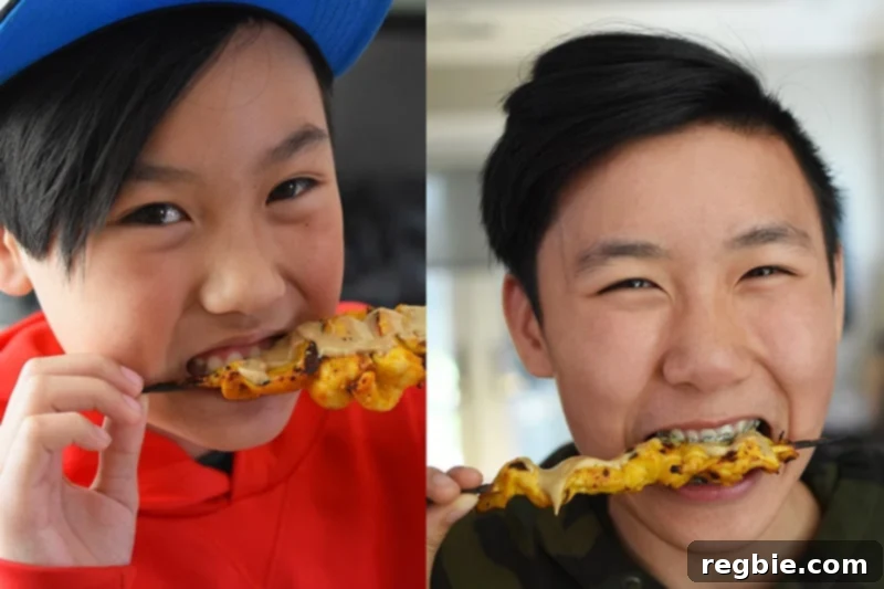Two smiling boys biting into paleo chicken satay skewers, showing how much kids love this healthy dish.