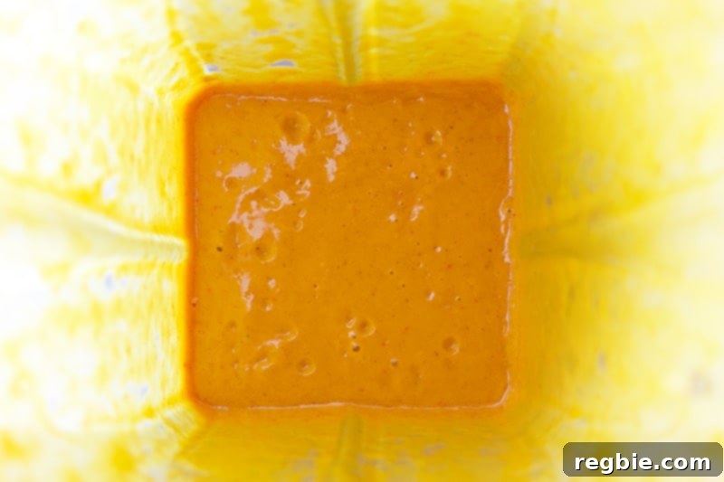 An overhead shot of the finished bright orange chicken satay marinade in the blender, showing its smooth consistency.