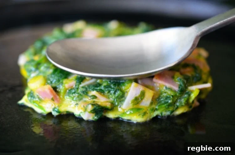 Wholesome Whole30 Keto Egg Foo Young 8 An Egg Foo Young (Spinach, Egg, Ham & Coconut Pancakes) is being fried on a cast iron skillet.