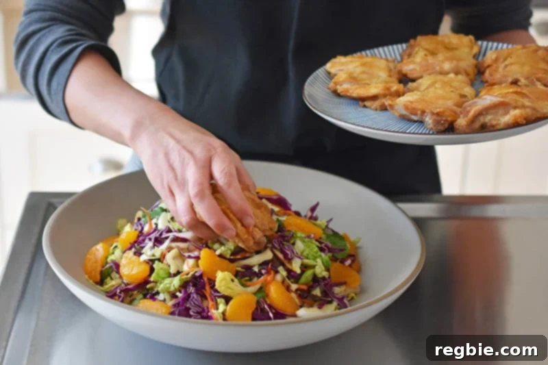 A person is placing sliced crispy chicken thighs on top of the Whole30 Chinese Chicken Salad