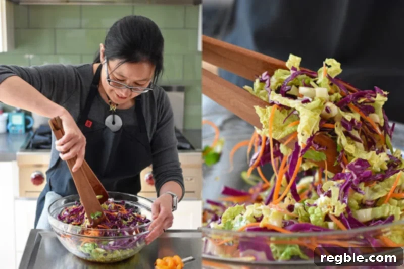 A woman is tossing Whole30-friendly Chinese Chicken Salad in a large clear bowl with wooden tongs.