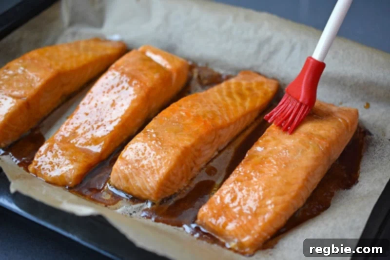 A basting brush is applying the reserved 'fresh' All-Purpose Stir-Fry Sauce onto the hot easy teriyaki salmon, enhancing its flavor and shine.