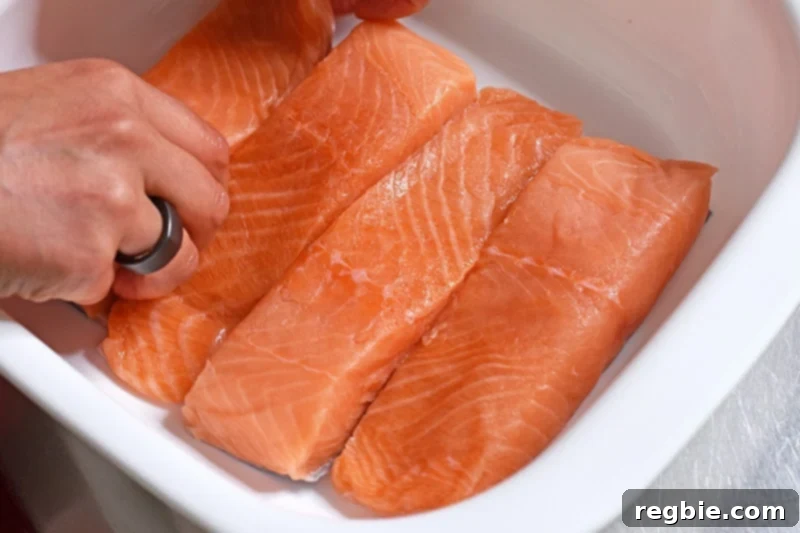 Four salmon fillets are neatly arranged in a snug-fitting white dish with high sides, ready for marination.