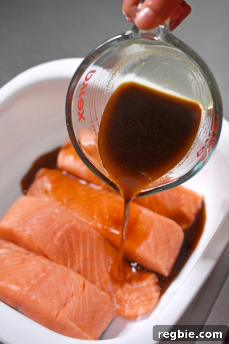 Generously pouring the All-Purpose Stir-Fry Sauce over the salmon fillets, initiating the marination for a healthy Whole30 teriyaki dinner.