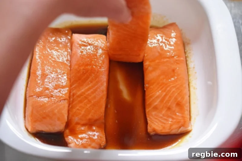 A hand is carefully flipping the salmon fillets to ensure they are fully coated in the All-Purpose Stir-Fry Sauce for optimal flavor absorption.