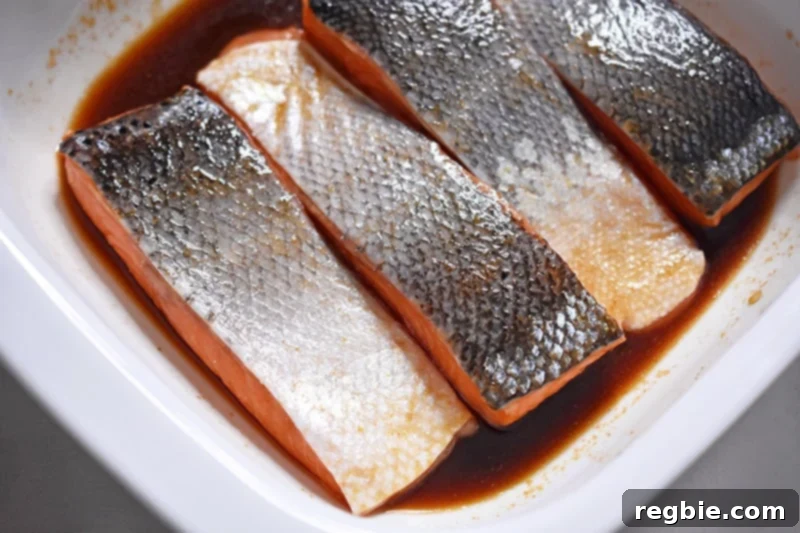 Salmon fillets marinating skin-side up in a Whole30-friendly teriyaki sauce, absorbing flavors for a delicious meal.