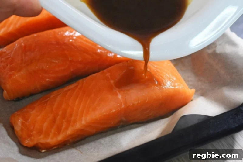 Pouring additional marinade from the dish over the salmon fillets on the baking sheet, enhancing the flavor before baking.