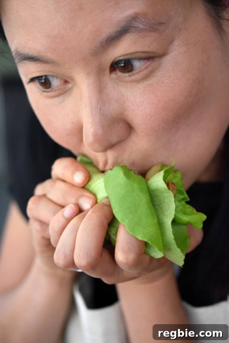 Classic Korean BBQ Kalbi 5 An Asian woman is biting into a lettuce wrap filled with Whole30 galbi, kimchi, and cauliflower rice. It's Paleo Korean food!