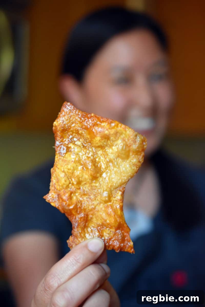 A woman holding a piece of crispy chicken skins cooked in an air fryer, highlighting the golden brown, crunchy texture.