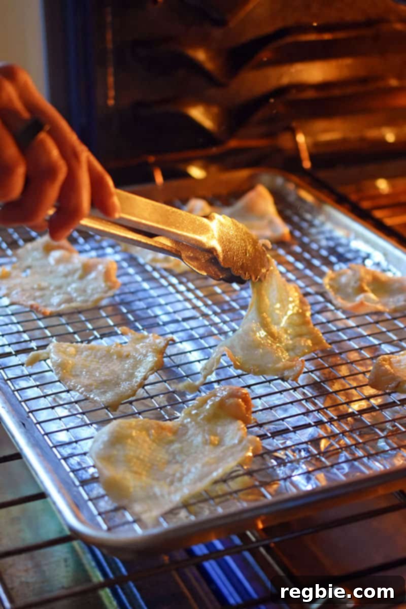 A person is using a pair of tongs to flip over chicken skins that are baking in the oven for even crisping.