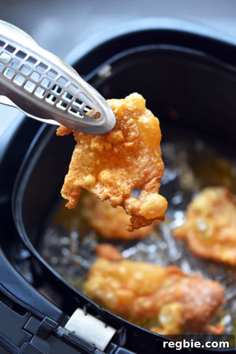 A pair of tongs are removing crispy chicken skins from an air fryer, ready to be cooled.