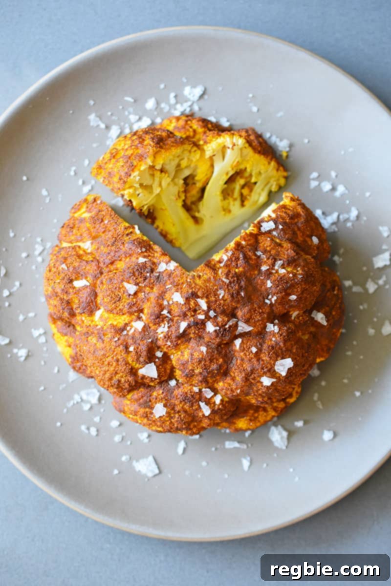 An overhead shot of Tandoori Whole Roasted Cauliflower on a brown plate with a wedge sliced out of it, garnished with fresh herbs.