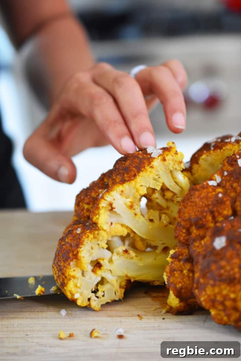 Someone expertly slicing into a beautifully roasted Tandoori Whole Roasted Cauliflower, preparing it for serving.
