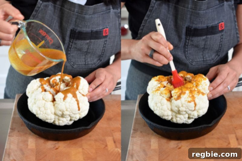 Someone pouring and brushing creamy Tandoori marinade onto the bottom of a whole cauliflower head in a roasting pan.
