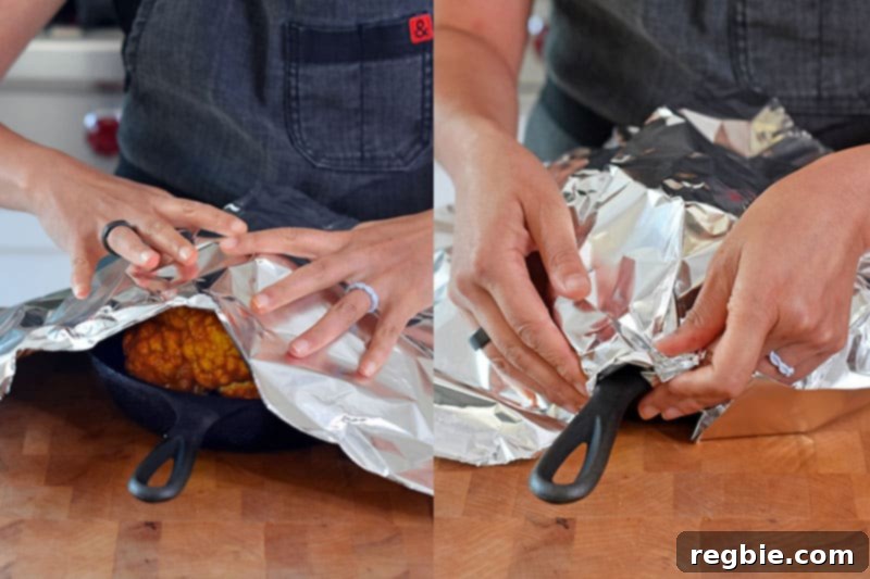 Someone carefully covering the Tandoori Whole Roasted Cauliflower with aluminum foil in its roasting pan, preparing it for the oven.