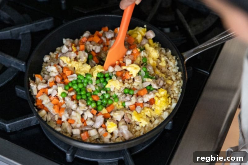 Mixing in the peas, chicken, scrambled eggs, and vegetables into low carb cauliflower chicken fried rice.