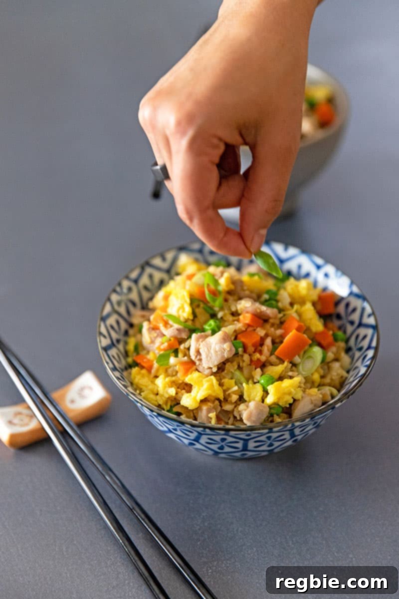 Someone adding scallions to a bowl filled with healthy cauliflower chicken fried rice.