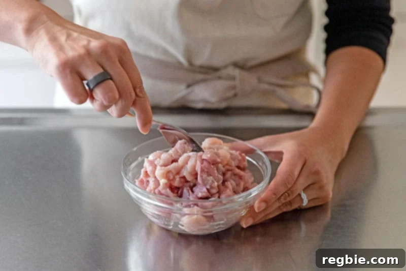 Someone is mixing diced raw chicken with oil and seasonings for healthy cauliflower chicken fried rice.