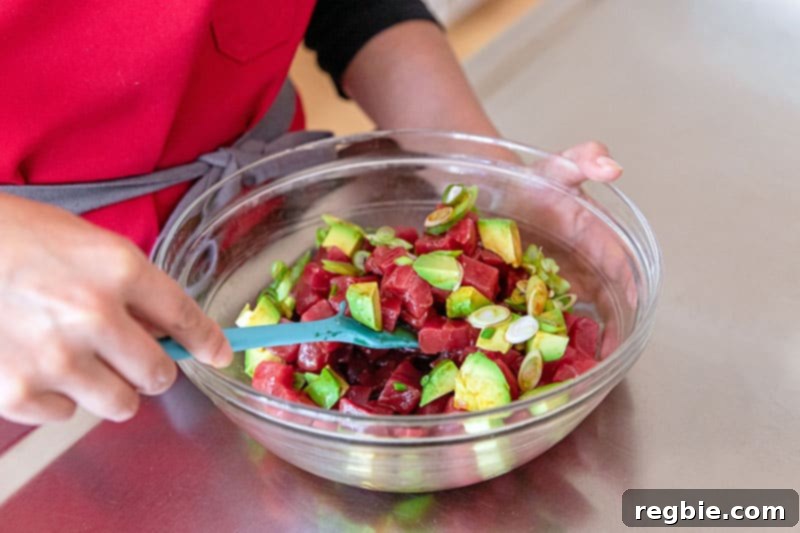 Clean Eating Tuna Avocado Poke 8 A person is carefully mixing the tuna poke with avocado in a bowl, ensuring the sauce is evenly distributed without crushing the ingredients.