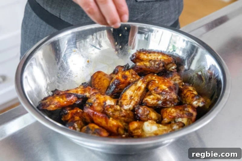 Generously sprinkling toasted sesame seeds over freshly tossed Whole30 Chinese Chicken Wings, adding a delightful crunch and finish.