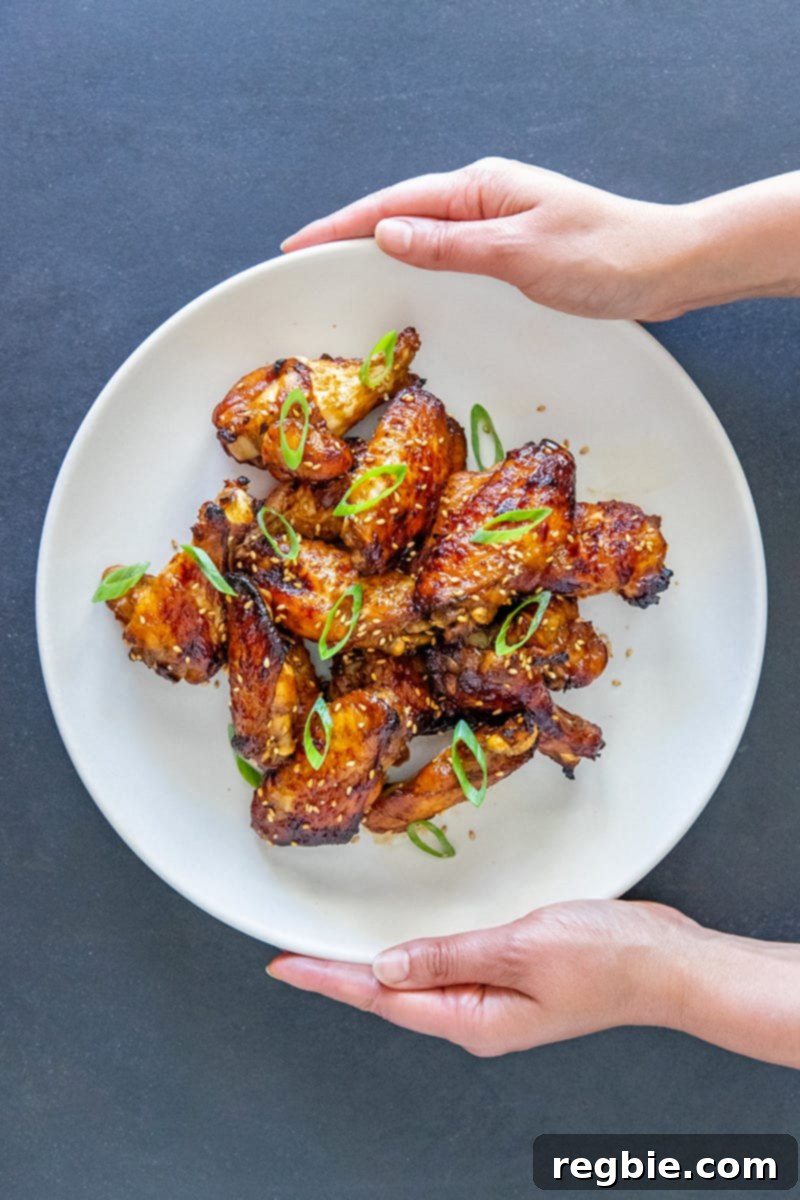 Two hands holding a generously loaded platter of perfectly cooked, Whole30 and Paleo-friendly Chinese Chicken Wings, ready for serving.