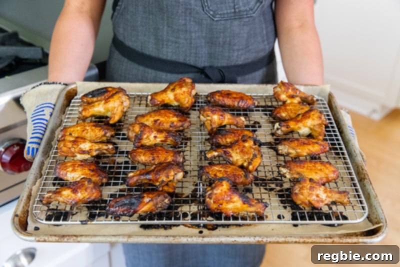 A hand holding a tray of freshly baked, gluten-free, sticky Chinese Chicken Wings, glistening and ready to be served from the oven.