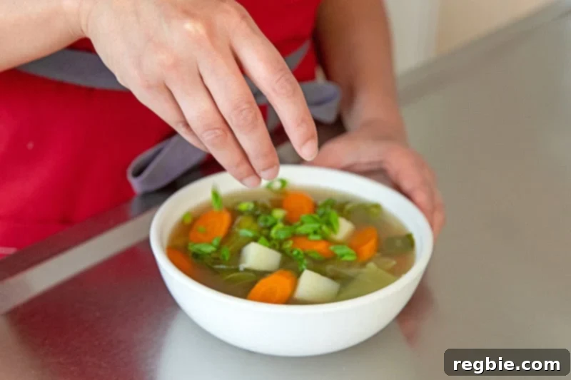 Sprinkling vibrant sliced scallions on top of a hot bowl of Instant Pot Vegetable Soup, adding a final fresh touch.