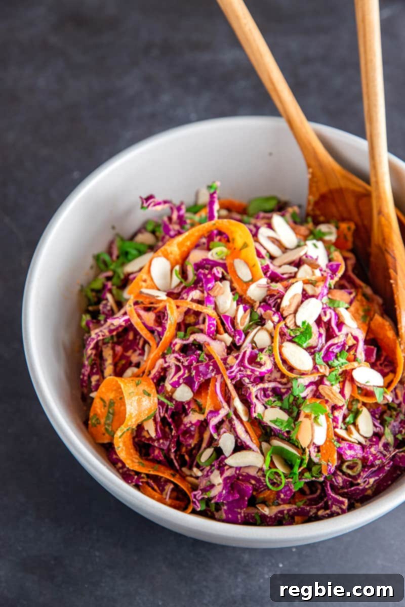 Bright Red Cabbage Slaw with Zesty Ginger Carrot Dressing 2 A large white bowl filled with colorful Whole30 and paleo red cabbage slaw, garnished with fresh herbs and two wooden serving spoons, ready to be served.