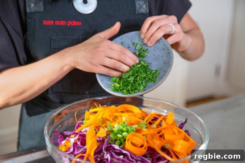 Bright Red Cabbage Slaw with Zesty Ginger Carrot Dressing 6 A shot of someone adding freshly chopped cilantro and thinly sliced green onions to a large bowl already filled with vibrant red cabbage and shredded carrots, preparing the base for the red cabbage slaw.