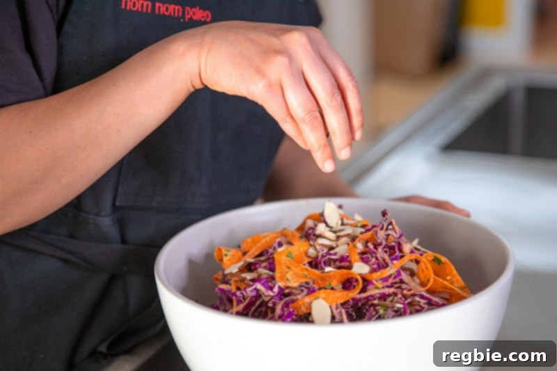 Bright Red Cabbage Slaw with Zesty Ginger Carrot Dressing 8 The final touch: perfectly toasted slivered almonds being sprinkled generously on top of the vibrant Whole30 and paleo red cabbage slaw, adding a delightful crunch and garnish.