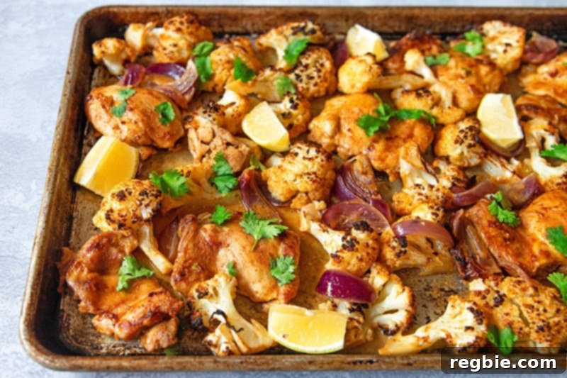 An overhead view of sheet pan Tandoori Chicken fresh from the oven with lemons and cilantro on top.