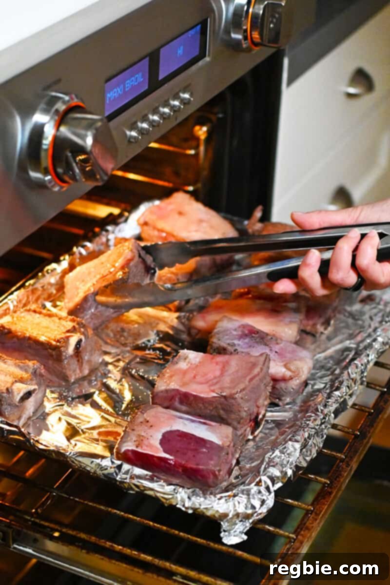 Fall-Off-The-Bone Slow Cooker Korean Short Ribs 9 An open oven with someone flipping broiled beef short ribs over on a rimmed baking sheet.