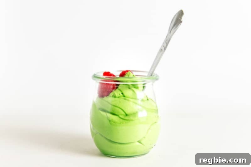 Creamy Paleo Dairy Free Matcha Pudding 13 A tempting side profile of dairy-free matcha pudding presented in a clear glass, with a spoon resting invitingly inside, garnished with fresh raspberries.
