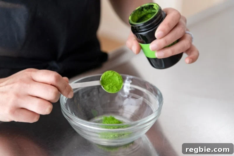 Creamy Paleo Dairy Free Matcha Pudding 3 Someone carefully spooning vibrant green matcha powder into a small white bowl, preparing it for the paleo matcha pudding recipe.