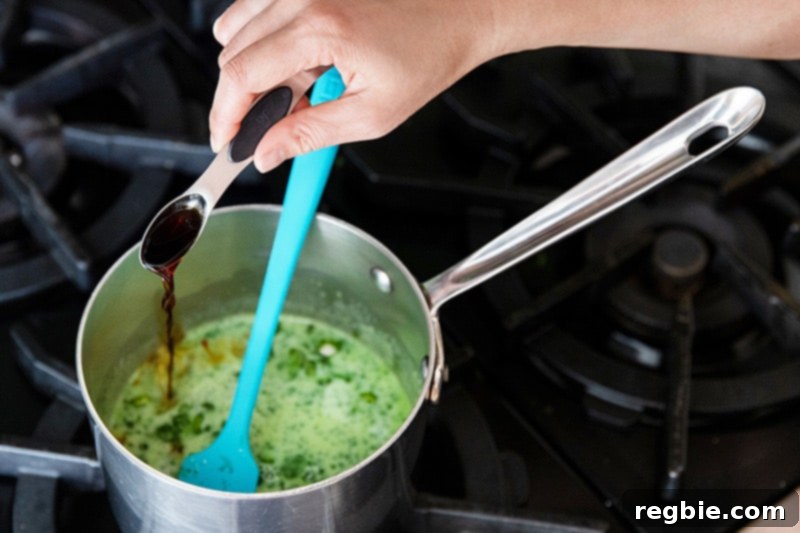 Creamy Paleo Dairy Free Matcha Pudding 8 A stream of clear vanilla extract being poured into a small saucepan containing the warm, green coconut matcha milk, adding the final flavor touch.
