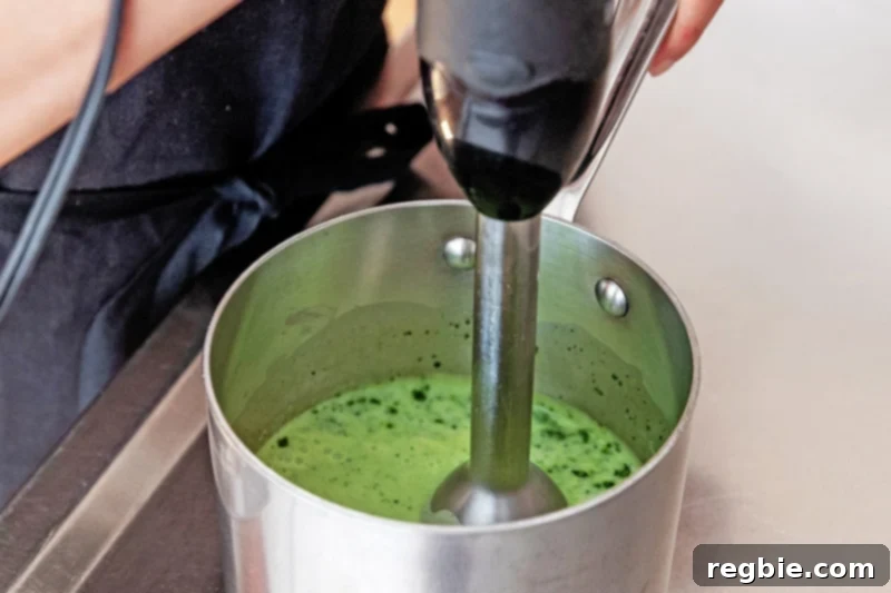 Creamy Paleo Dairy Free Matcha Pudding 9 An immersion blender actively blending the matcha and coconut milk mixture in a small saucepan, ensuring a perfectly smooth and uniform consistency for the pudding.