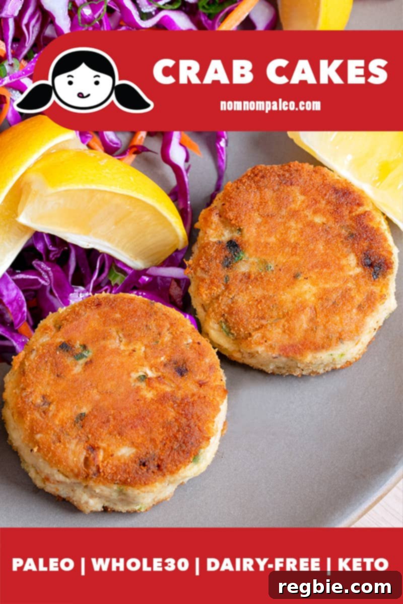 Two golden brown paleo crab cakes are on a beige plate, next to purple cabbage slaw and lemon wedges.