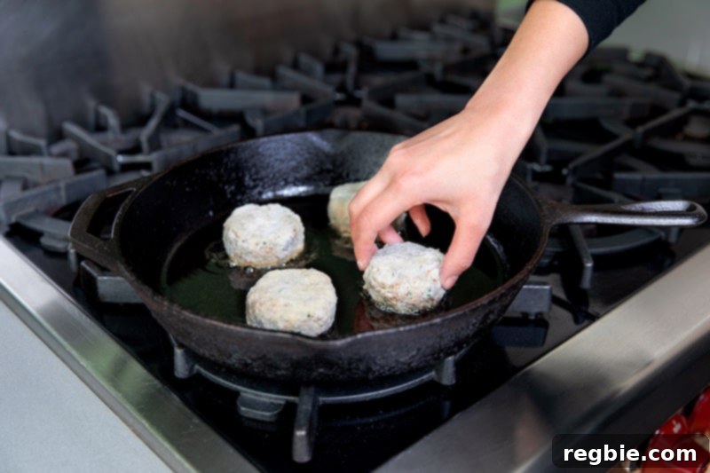 Adding paleo crab cakes to a cast iron frying pan.