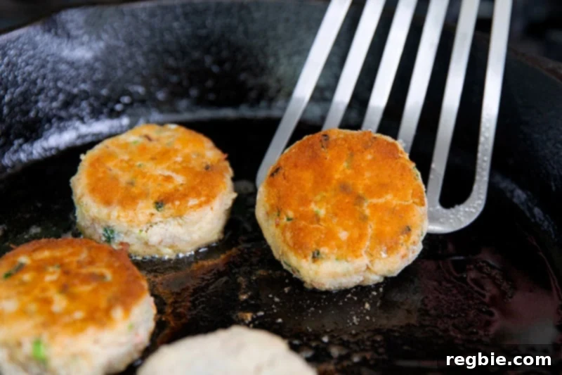 Flipping golden brown paleo crab cakes in a cast iron skillet with a metal fish spatula.