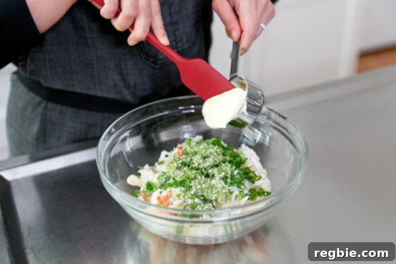 A large glass bowl filled with crab, scallions, coconut flour, seafood seasoning, and mayonnaise.