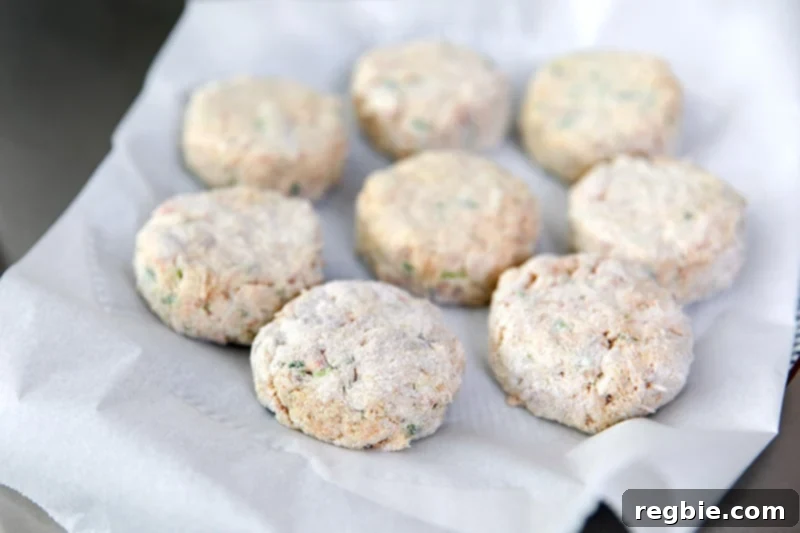 A parchment paper lined plate is filled with paleo crab cakes that are waiting to be fried.