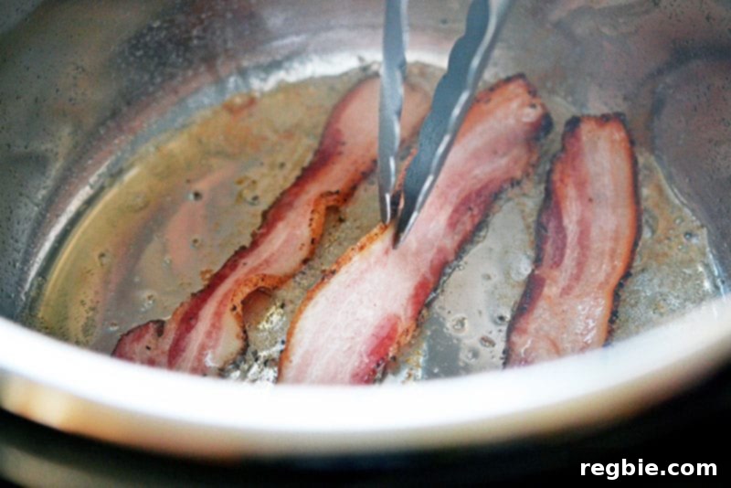 Three slices of bacon sizzling in the bottom of an Instant Pot, providing a smoky base for the Kalua Pork.