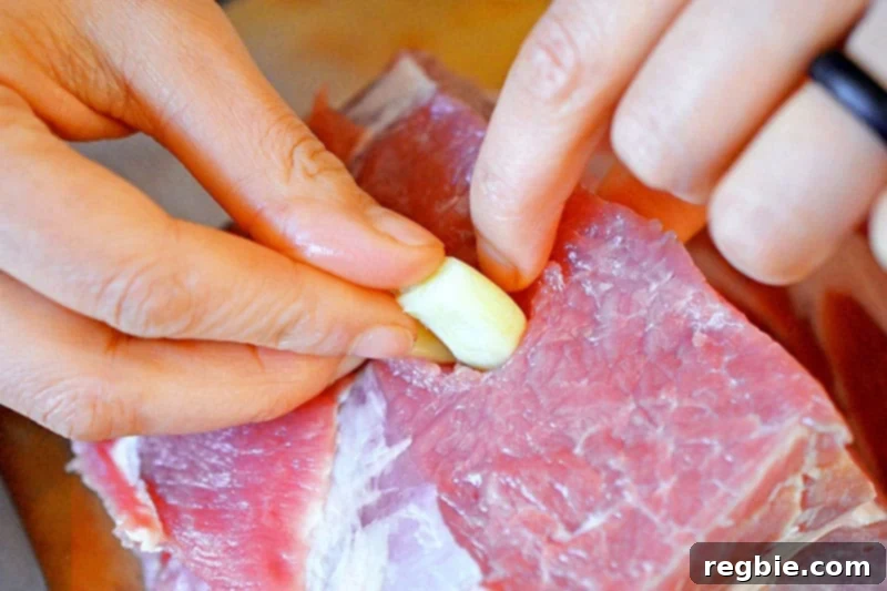 Tucking peeled garlic cloves into small slits made in the pork shoulder roast, enhancing its flavor.