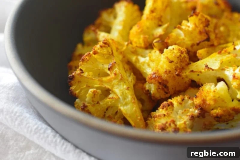 A close-up view of a vibrant blue bowl filled with tender, golden-brown roasted curried cauliflower, garnished with fresh green herbs.